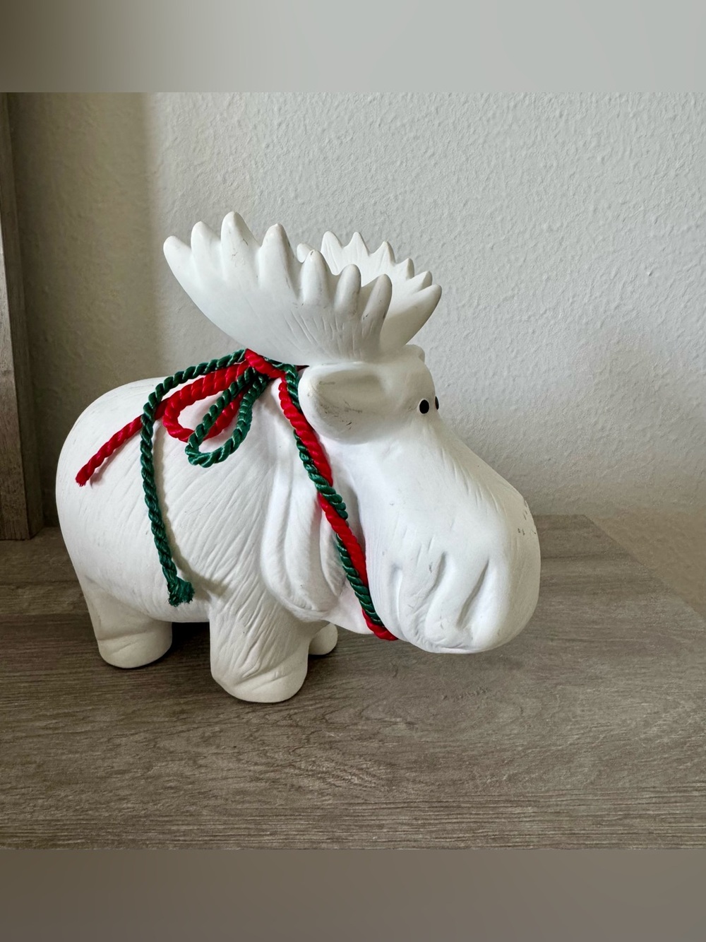 A minimalist white ceramic moose figurine with a Christmas ribbon—festive decor
